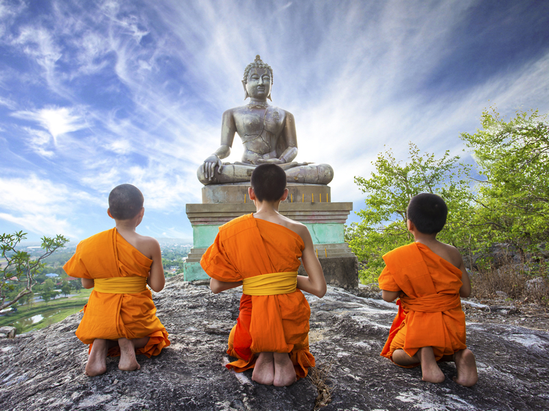 Buddha heykelinin önünde sırtı dönük diz çökmüş çocuklar rahipler