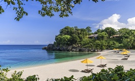 Boracay'da sarı plaj şemsiyeleri ve beyaz kumsalda ağaçların arasından görünen Banyugan plajı