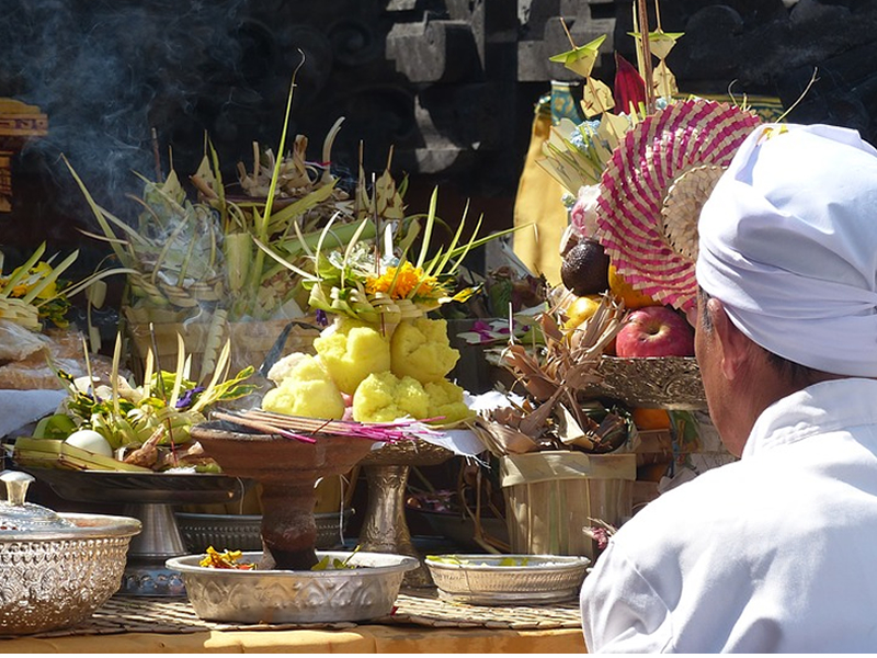 Meyveler ve tütsülerin olduğu bir tezgah önünde arkası dönük beyazlar giyinmiş dua eden adam
