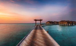 Gün batarken pembe olan gökyüzü altında iskeleden görünen su üstü bungalovlar Maldivler