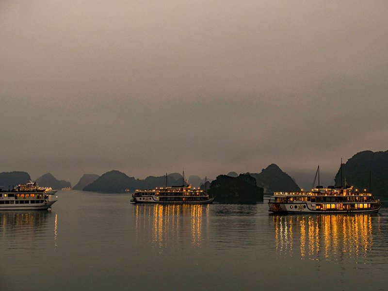 Vietnam Halong körfezindeki teknelerin gece suya yansıyan ışıkları ile görüntüsü