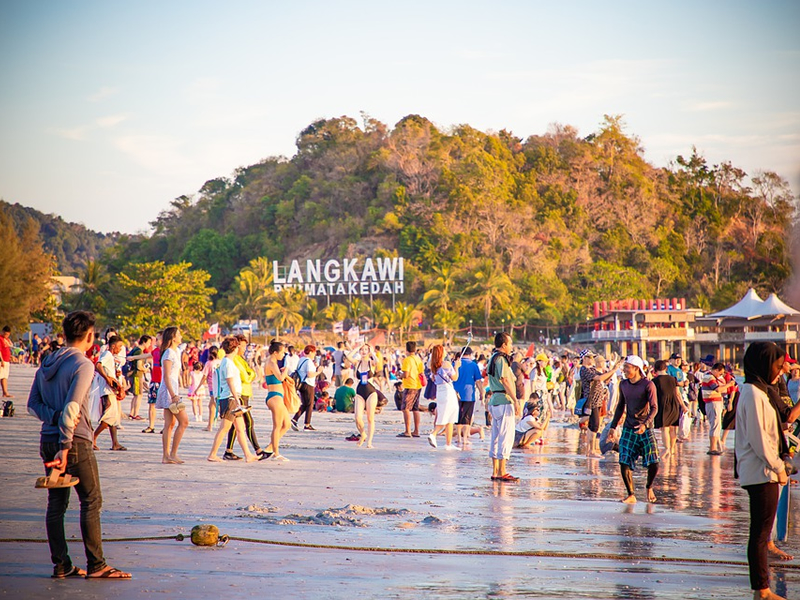 Arkadaki dağ üzerinde Langkawi yazısı ve sahilde bir çok insan