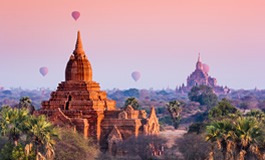 Akşam üstü güneş batarken pembe renge bürünmüş gökyüzü altında uçan balonlar ve Bagan'daki Pagoda